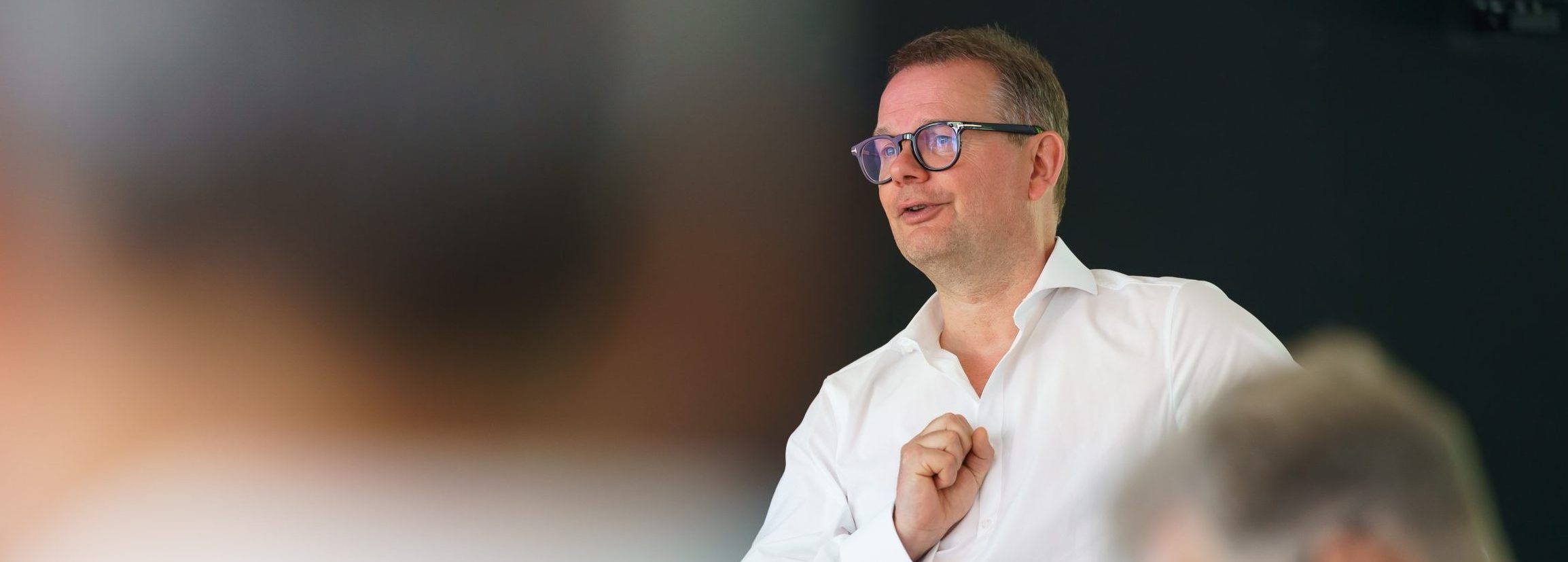 Man with glasses in a white shirt speaking to an audience