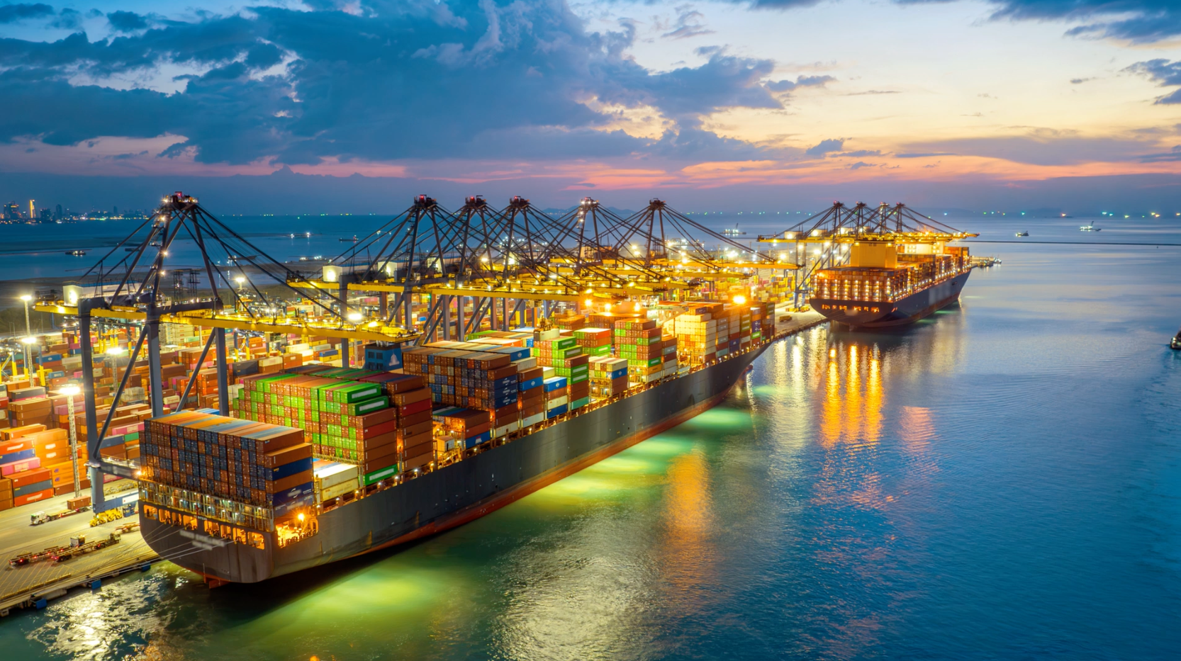Container ship with cargo at illuminated harbour cranes at dusk