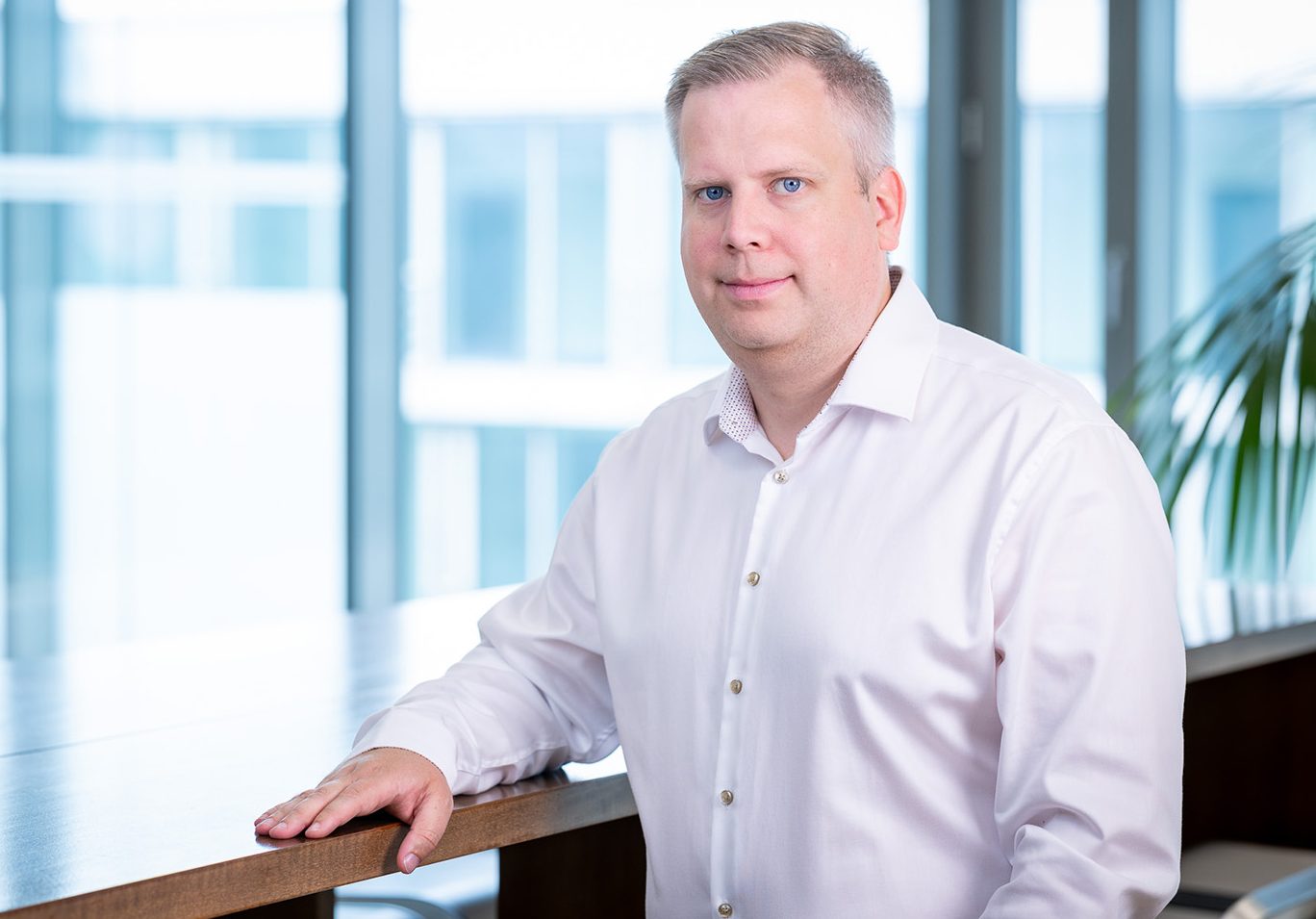 Portrait of a man in a white shirt at a wooden table in a bright office