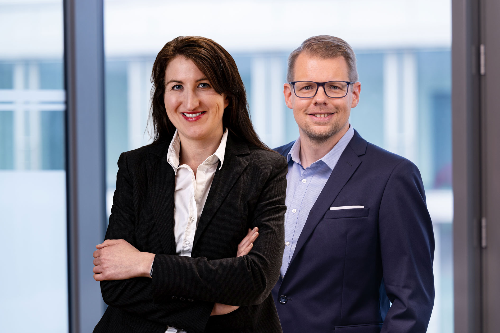 Portrait of a woman and a man in business attire in front of large windows