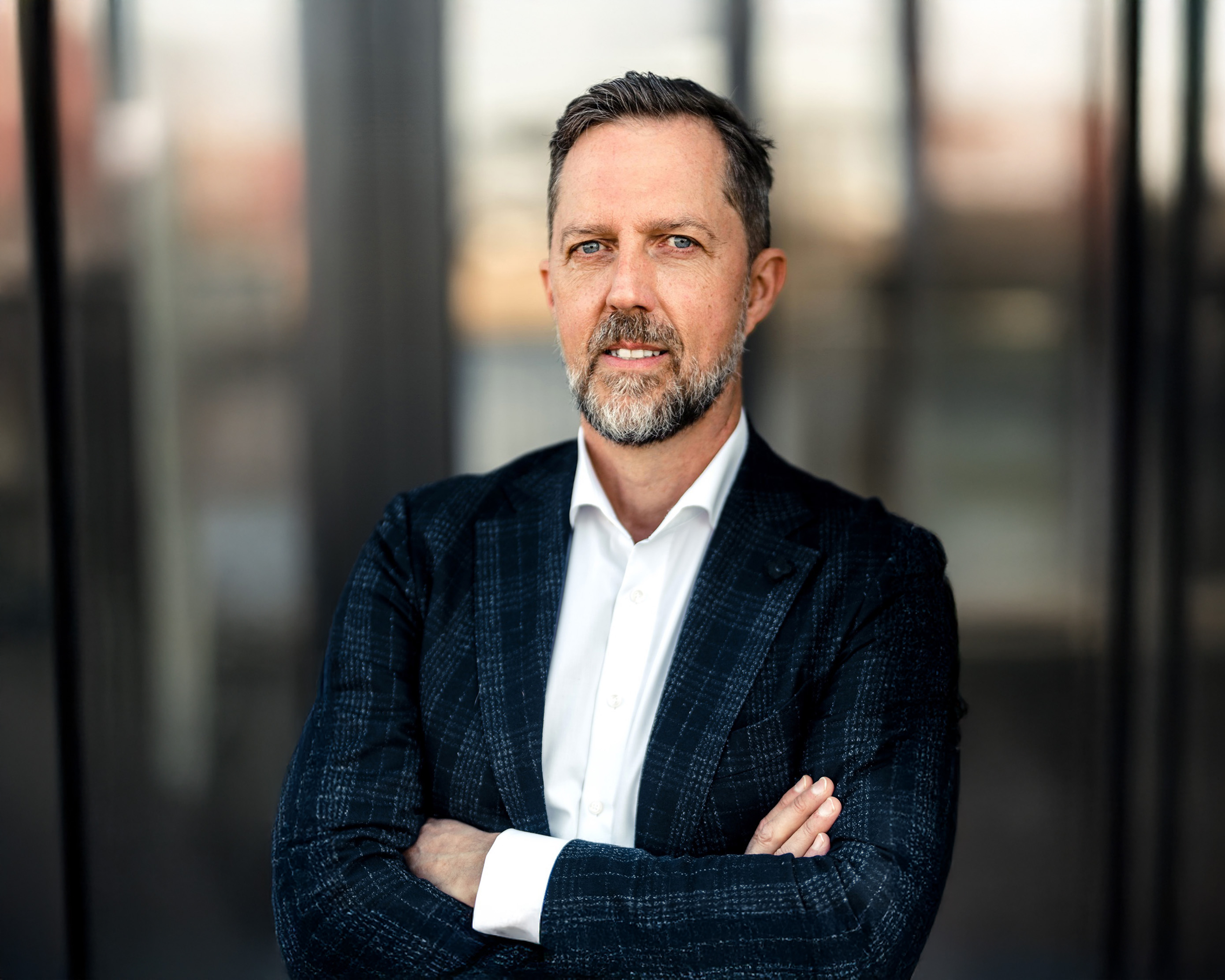 Portrait of a bearded man in a checked jacket in front of a glass facade