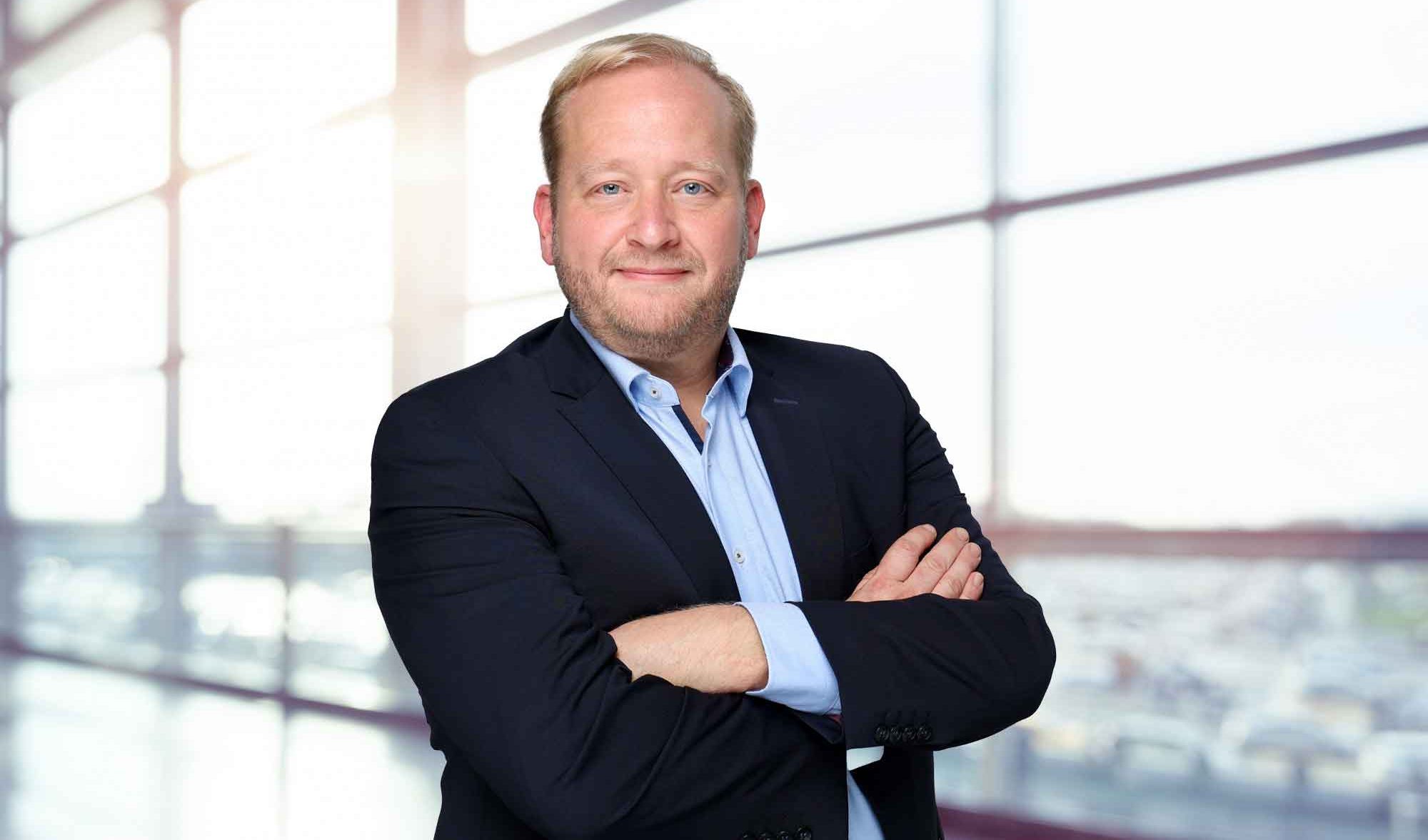 Portrait of a man in a dark suit and light blue shirt in front of an office building