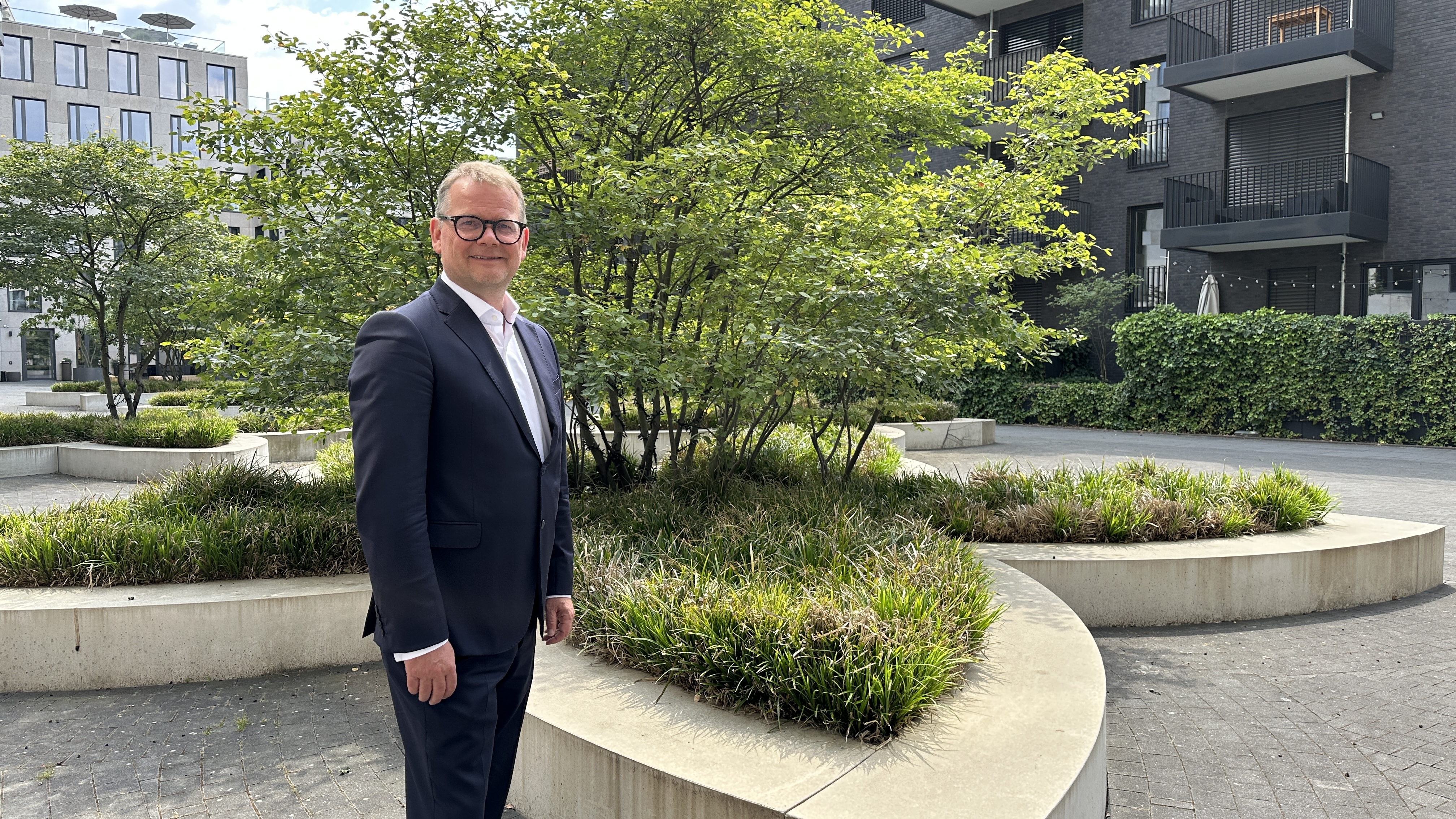 Man in a dark suit standing in a green city park